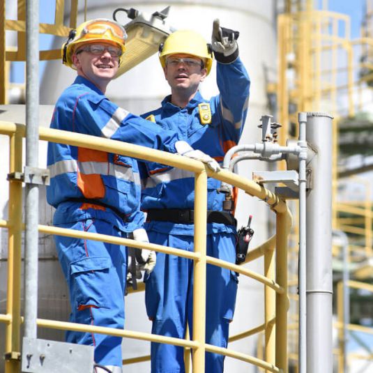 Industrial plant construction: Workers wearing helmets and high-visibility vests use tablet with app in industrial plant.