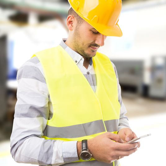 Site manager with cellphone and yellow safety helmet.